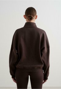 Sudadera marrón de gran tamaño con cuello alto y hombros caídos, hecha de un tejido suave y texturizado. Puños y dobladillo ajustados.