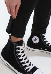 Černé vysoké tenisky z plátna s bílými tkaničkami, s kulatou logovou nášivkou a kontrastními bílými gumovými podrážkami.