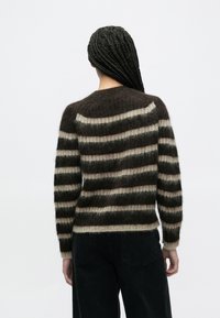 Pulover în dungi, în tonuri de maro închis și bej, confecționat dintr-un material moale și pufoș. Prezintă un guler rotund și mâneci lungi.