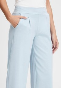 Lichtblauwe wijde broek met een gladde stofstructuur, voorzien van een aansluitende tailleband, plooien en zijzakken voor functionaliteit.