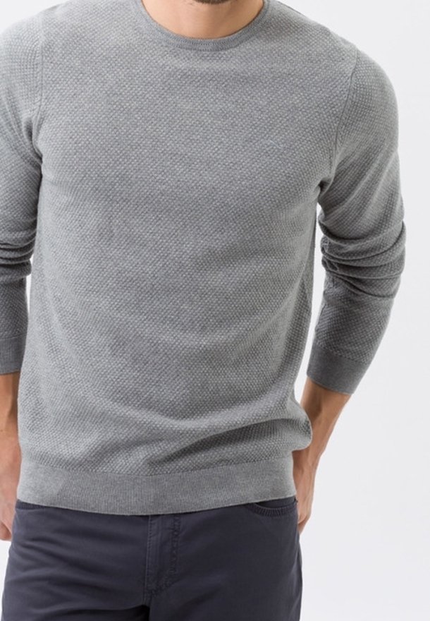 Pull en maille grise texturé avec un col rond et des manches longues. Le tissu présente un motif subtil et est assorti à un pantalon sombre.