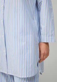Lichtblauw en wit gestreept shirt met een kraag, lange mouwen en knoopsluiting. Heeft een zijsplit en een zachte katoentextuur.
