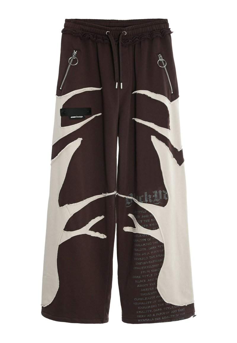 Pantalones de pierna ancha en marrón oscuro y crema con patrones de árboles abstractos, bolsillos con cremallera y cintura ajustable con cordón. Detalles de texto en la parte inferior de la pierna.