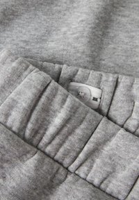 Grå sweatshirt-tyg med en mjuk, texturerad yta. Har ett samlat midjeband med en vit etikett och synliga sömnadsdetaljer.