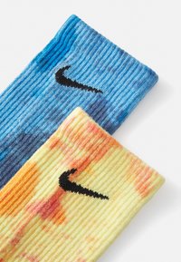 Modré a žlté ponožky s motívom tie-dye s čiernymi logami Nike. Rífľová textúra, výrazné prechody farieb a gradienty sú prítomné na každej ponožke.