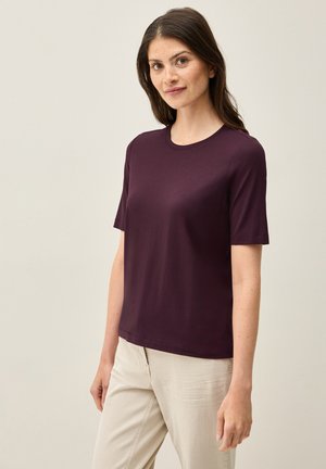 Short-sleeve, crew neck T-shirt in deep plum color, made of smooth fabric. Simple cut, no patterns or embellishments. Paired with light trousers.