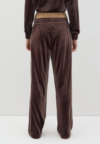 Pantalones de chándal de terciopelo marrón con cinturilla elástica y corte relajado, que presentan una textura suave y un diseño de pierna ligeramente acampanada.