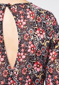 Gros plan sur le dos d'une robe à motif floral avec une ouverture en forme de goutte d'eau fermée par un bouton recouvert de tissu au niveau de l'encolure.