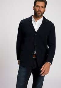 Blazer de mezcla de lana azul marino con cuello con muesca, dos bolsillos frontales y cierre de tres botones, superpuesto a una camisa blanca con cuello y jeans de mezclilla oscuros.