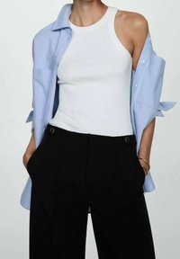 Débardeur blanc sans manches associé à une chemise boutonnée bleu clair et à un pantalon noir taille haute avec des poches latérales et des accents en anneau.