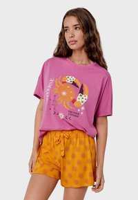 Roze katoenen t-shirt met een krab graphic en tekst, gecombineerd met oranje shorts met een zonnenpatroon. Losse pasvorm en casual stijl.