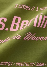 Zöld anyag pink szöveggel, amely a következőket említi: "3 város // 1 éjszaka," "S. Berlin," "Columbia Waves," valamint zenei műfajokat, beleértve az elektronikus és indie zenét.