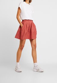 Gonna di lino rosa con vita arricciata, due tasche laterali e forma svasata, abbinata a una maglietta bianca e scarpe da ginnastica bianche.