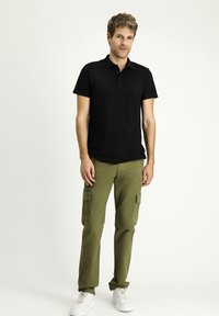 Polo shirt negro de manga corta, material de algodón, con botones en el frente, combinado con pantalones cargo verdes oliva con bolsillos laterales y zapatillas blancas.