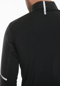 Sort atletisk top med høj krave, med reflekterende detaljer på ryggen og ærmerne, glat tekstur og tætsiddende design.