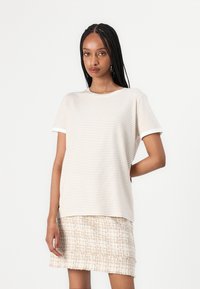T-shirt beige a righe con maniche corte e colletto rotondo, abbinato a una gonna di tessuto intrecciato di colore chiaro. Tessuto morbido, vestibilità rilassata.
