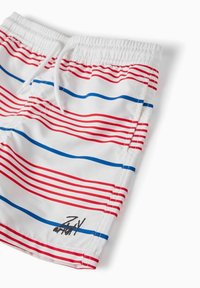 Shorts da mare bianchi con righe orizzontali rosse e blu. Presentano un elastico in vita con coulisse e un piccolo logo ricamato.