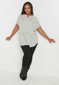 Camicia bianca a manica corta con pois neri, dotata di colletto a punta. Abbinata a jeans skinny neri e stivali neri al di sopra del ginocchio.