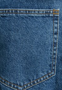 Blue denim fabric with a standard back pocket, featuring contrasting orange stitching along the seam and edges. Texture is slightly coarse.