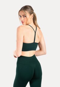 Sujetador deportivo verde oscuro con tirantes ajustables y espalda con abertura, combinado con leggings de cintura alta en color a juego y tejido texturizado.