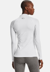 Long-sleeve athletic top in white, featuring a high collar, seamless design, and subtle stitching details. Textured fabric for breathability.
