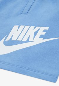 Ανοιχτό μπλε μπλουζάκι Nike με μεγάλο λευκό λογότυπο και swoosh. Το ύφασμα έχει λεία υφή με ορατές ραφές κατά μήκος  των ακρών.