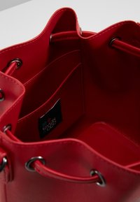 Rød læder spandtaske med en glat overflade, sølvfarvet hardware og indvendige lommer. Indeholder et mærke tag.