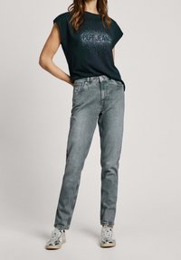 Camiseta negra de manga corta con el logo de "Pepe Jeans", combinada con unos vaqueros grises de pierna recta y zapatillas blancas con detalles metálicos.