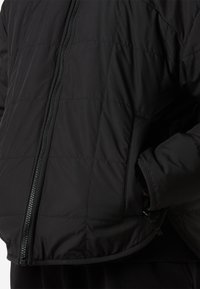 Μαύρο μπουφάν puffer με υφή καπιτονέ, κλείσιμο με φερμουάρ και πλαϊνές τσέπες. Το υλικό φαίνεται λείο και ελαφρώς γυαλιστερό.