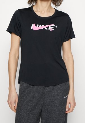 Osoba nosząca czarną koszulkę z przerobionym różowym logo Nike oraz ciemnoszare spodnie dresowe z małym białym znakiem Nike na lewej udzie.