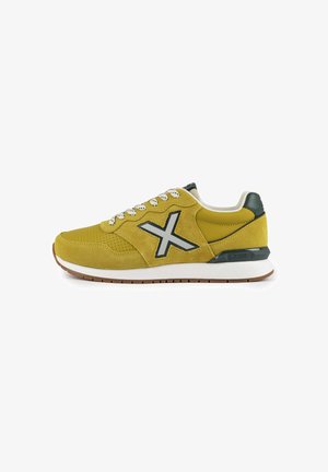Yellow suede athletic shoe with white laces, dark green accents, a large white 'X' logo on the side, and a light brown rubber sole.
