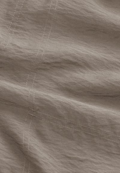 Gros plan sur un tissu beige avec des coutures visibles et de subtiles rides.