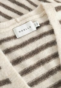 Gebreide trui in crème en taupe met strepen, voorzien van een stoffen label met de tekst "NOELLA" en een kleiner label met maat S/M, gemaakt in Italië.