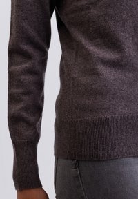 Hnědý pletený svetr s jemnou texturou, s manžetami a lemem s žebrováním. Materiál vypadá lehce a přiléhavě, zobrazuje detail rukávu.