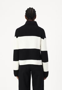 Maglione a righe bianche e nere con colletto alto, texture a costine e vestibilità ampia. Le maniche lunghe e la lunghezza cropped aumentano il comfort.