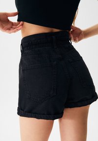 Černé riflové šortky s ohrnutým lemem, pružným pasem a dvěma zadními kapsami. Tkanina vypadá silná a hladká na dotek.