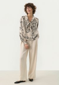 Beige blus med svart paisleymönster, med knytkrage och lång ärm. Matchas med lätta beige byxor och svarta ballerina.