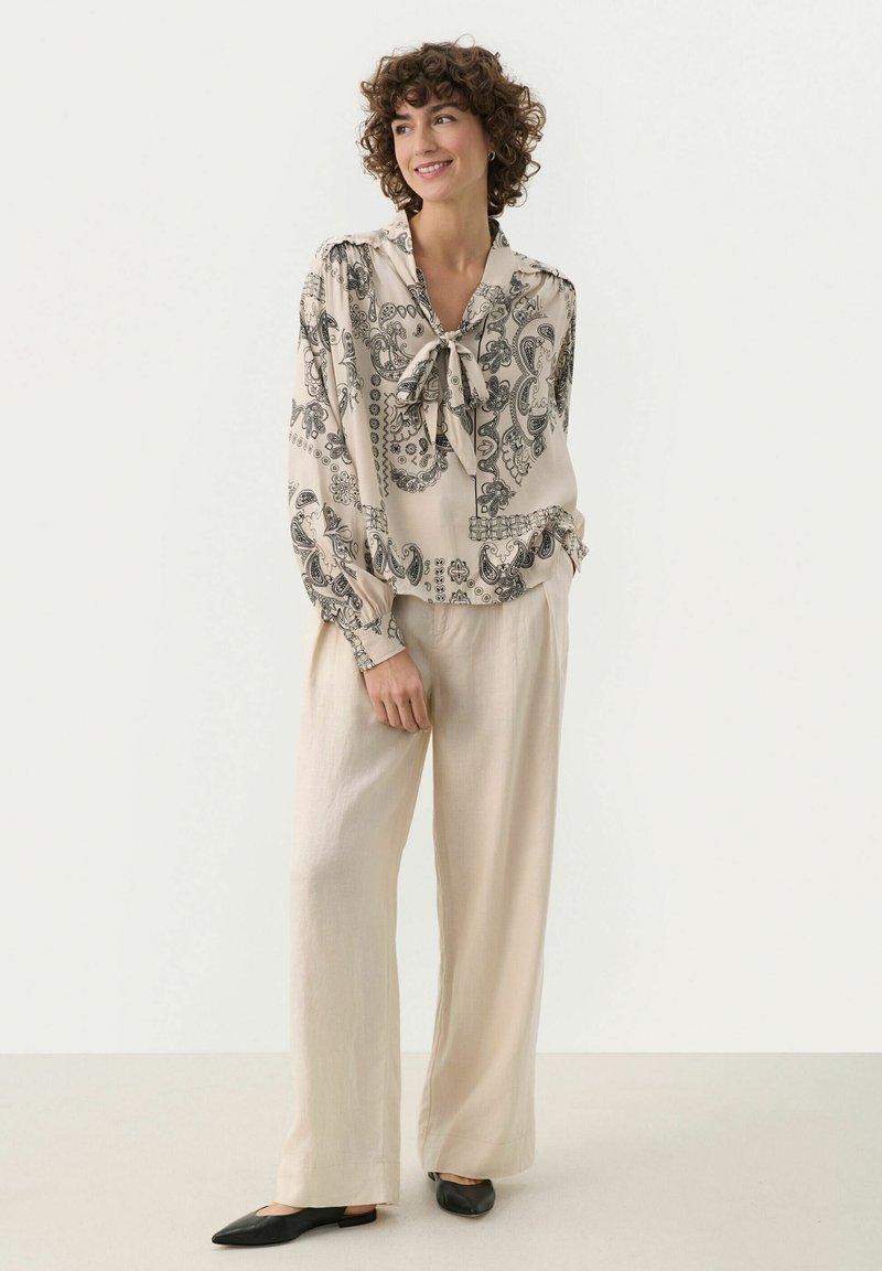 Beige blus med svart paisleymönster, med knytkrage och lång ärm. Matchas med lätta beige byxor och svarta ballerina.