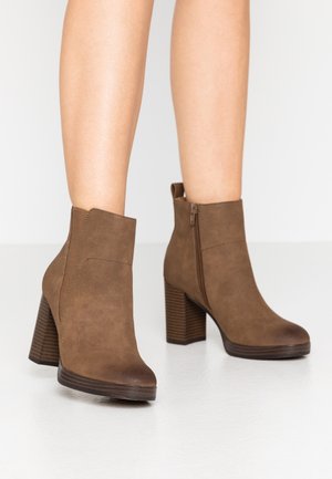 Bottines en faux suède marron avec un talon bloc, une fermeture éclair sur le côté et un bout rond. Les détails côtelés au niveau du talon ajoutent de la texture.