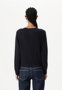 Navy crewneck sweater, knitted texture, long sleeves, ribbed hem, worn with dark denim jeans featuring classic back pockets and contrast stitching.