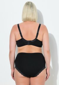 Černá podprsenka s krajkovými detaily a nastavitelnými ramínky, spárovaná s černými vysokými kalhotkami s vlnkovým krajkovým okrajem.