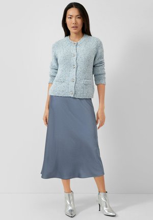 Jasnoniebieski dziany kardigan z długimi rękawami, pięcioma guzikami i dwiema kieszeniami, zestawiony z gładką, szarą spódnicą midi oraz srebrnymi botkami.