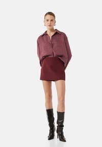 Yliresistentti maroon-raidallinen paita, jossa on nappilukitus, yhdistettynä tiukkaan maroon-minihameeseen ja polven yli ulottuviin mustiin nahkasaappaisiin.