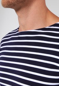 Marineblå og hvidstribet bomulds T-shirt med bådudskæring, der har jævnt fordelte striber og en blød tekstur. Nærbillede af udskæringen og skulderen.