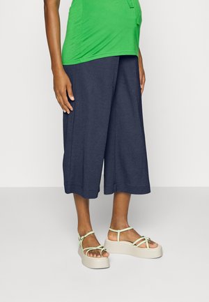 Top verde de mangas curtas combinado com calças cropped azul-escuras e sandálias de plataforma bege com tiras verde-claro. Textura de tecido suave.
