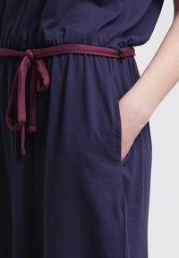 Granatowa, miękka sukienka z dopasowanym pasem, z burgundowym paskiem i bocznymi kieszeniami. Prosty, wygodny fason o luźnym kroju.