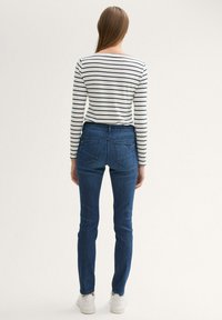Jeans de denim azul con un ajuste slim y cinco bolsillos, combinados con una camiseta de manga larga de rayas blancas y azules. Zapatillas blancas completan el look.