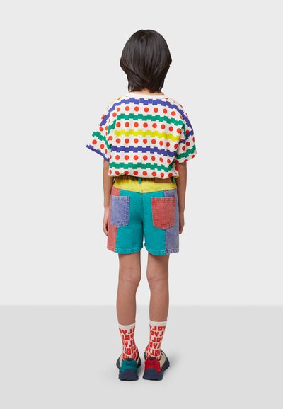 Chemise colorée à manches courtes avec des pois et des rayures, assortie à un short en patchwork turquoise, rouge et violet. Chaussettes blanches avec du texte rouge.