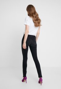 Pantalones vaqueros ajustados negros con una cinturilla de altura media, combinados con una camiseta blanca y tacones altos morados. Textura suave, diseño clásico de cinco bolsillos.