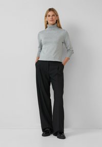 Pull en col roulé gris avec des manches côtelées associé à un pantalon noir à jambes larges. L'ensemble présente une texture lisse et une silhouette ajustée.